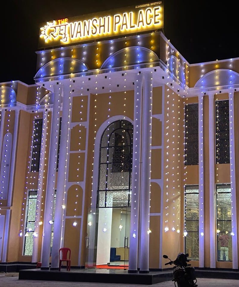 Illuminated front facade of Raghuvanshi Palace at night featuring string lights and rooftop neon signage