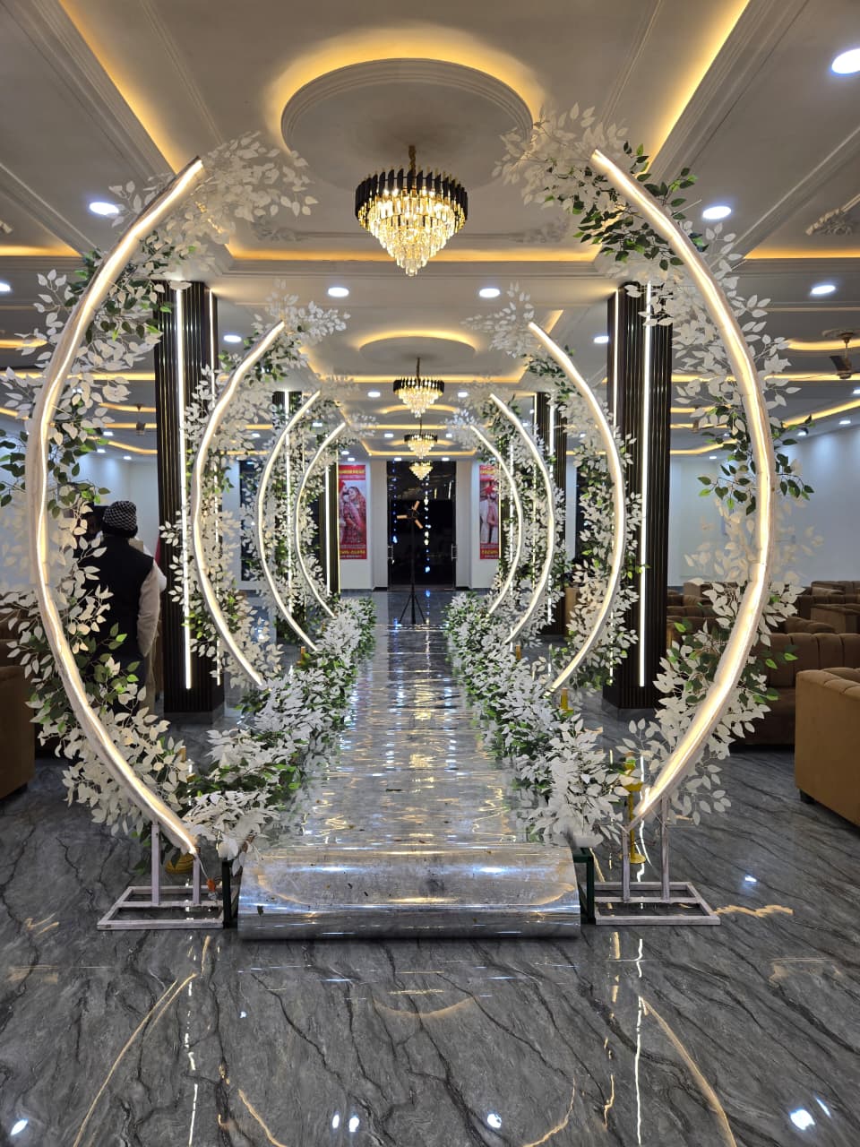 Wedding walkway with circular glowing floral arches and ceiling lights inside the hall
