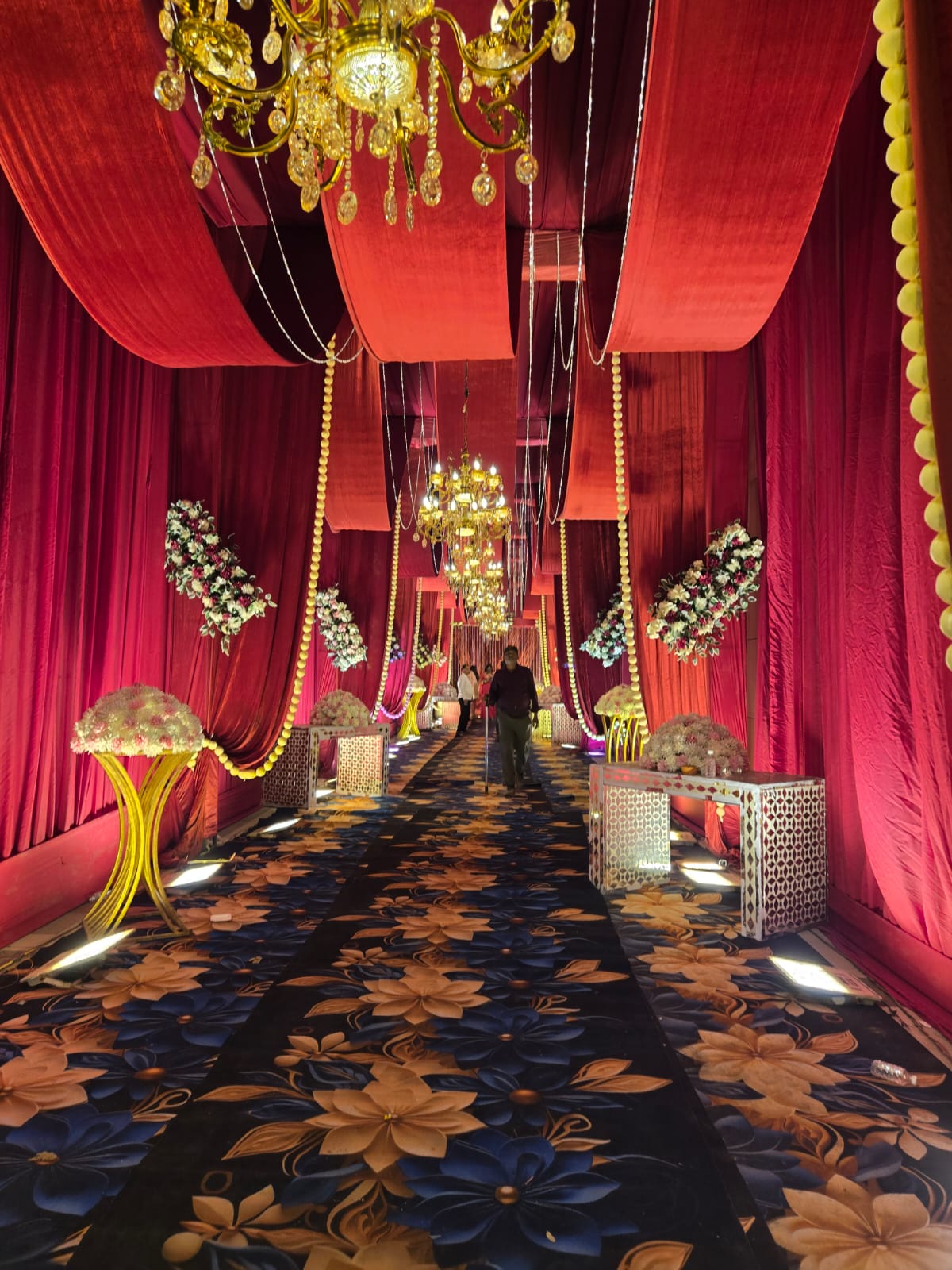 Wedding passage styled with rich red ceiling drapery, carpet, and floral arrangements