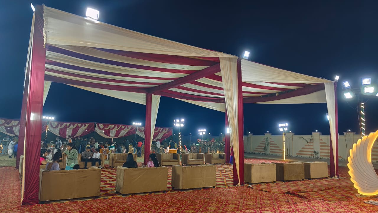 Outdoor lawn reception setup with striped red and cream canopy and evening lighting