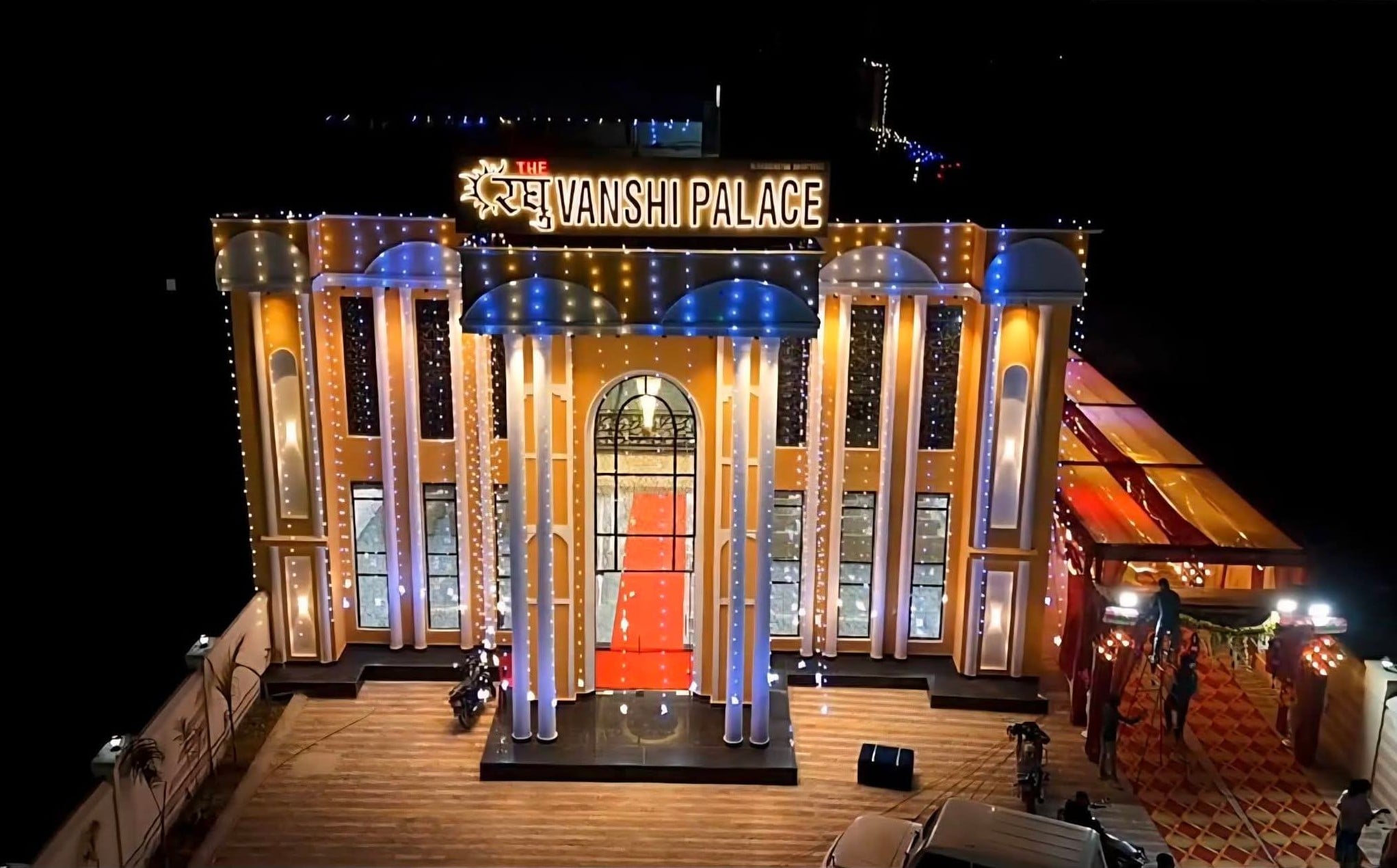 Exterior view of Raghuvanshi Palace illuminated at night with lights, golden pillars, grand entrance, and rooftop sign